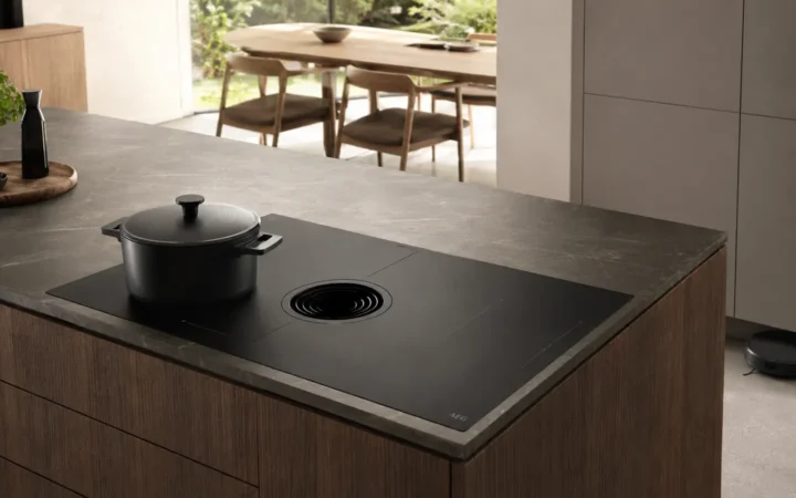 Editorial visualization of an induction pasta pot and slim robot vacuum in a modern kitchen