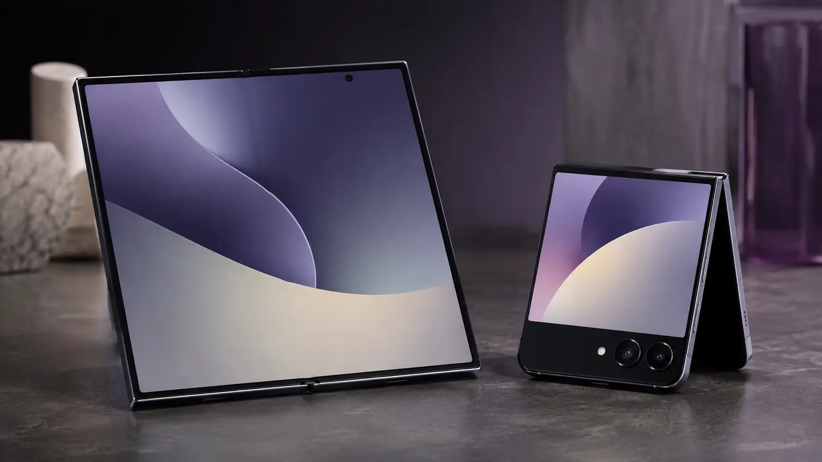Two foldable smartphones on a blue gradient surface, with one book-style foldable open beside a compact clamshell model in premium studio lighting