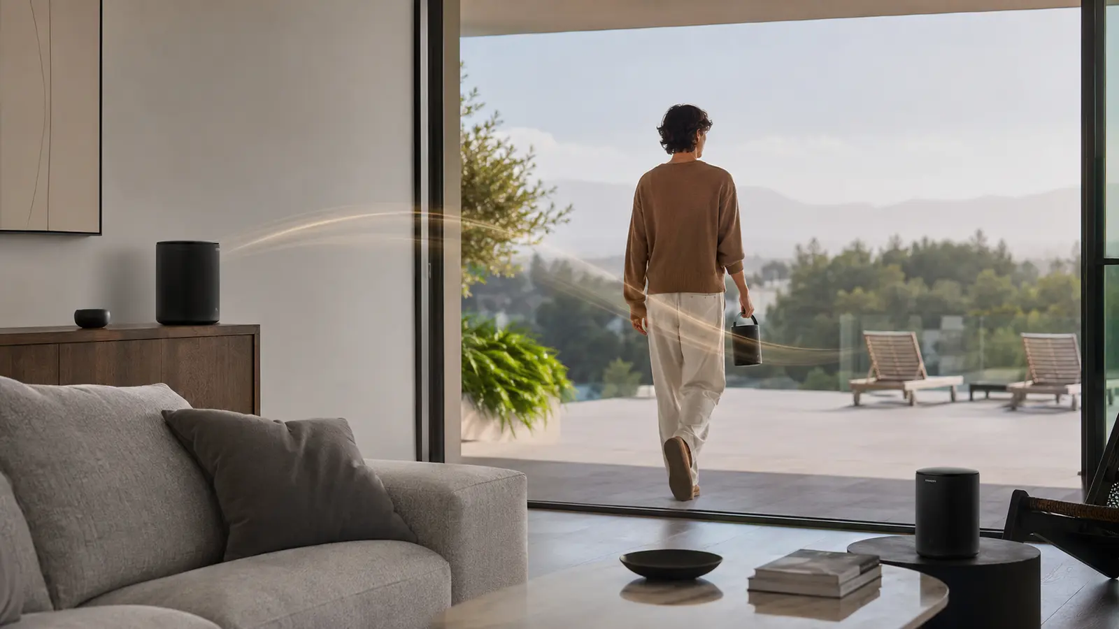 Person carrying a handled wireless speaker from a living room to a terrace