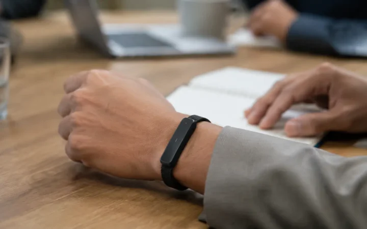 Editorial visualization of a slim black wearable recorder and fitness band beside a phone transcript