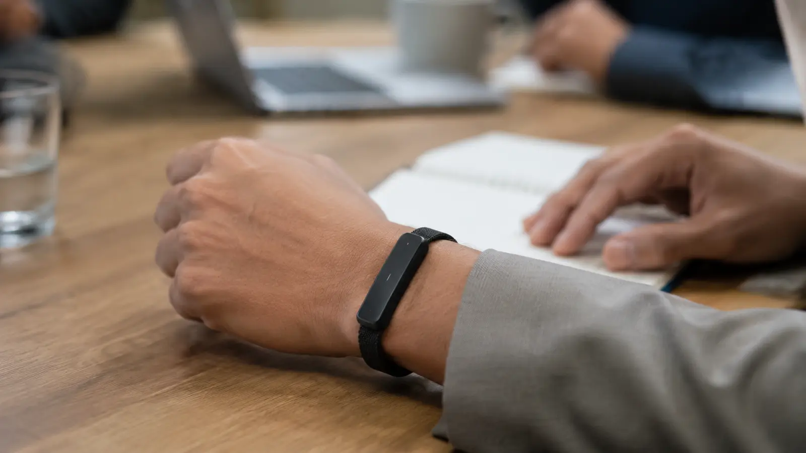 Slim black wristband-style recorder and fitness tracker beside a smartphone showing abstract transcript lines and waveform shapes
